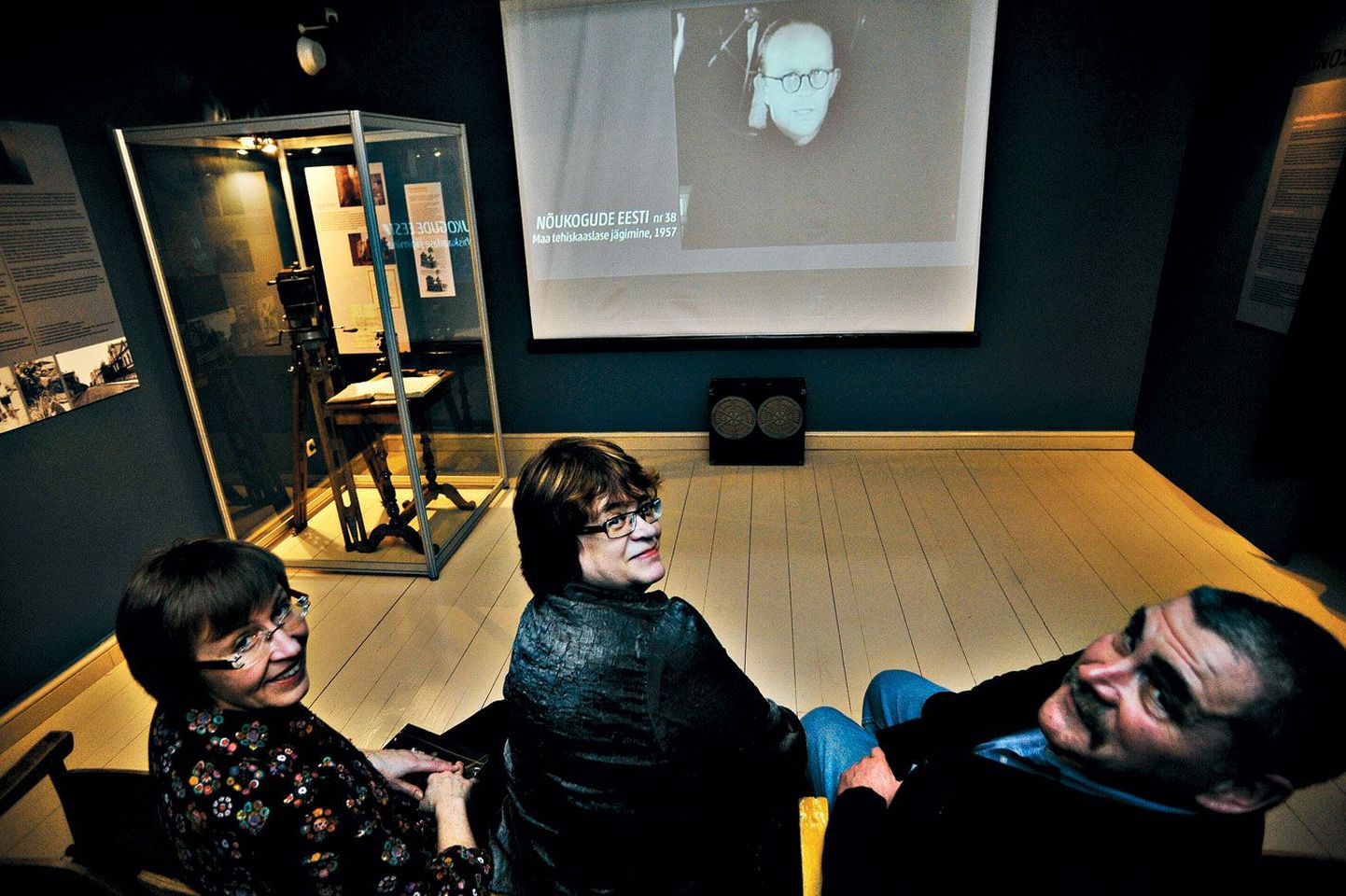 Filmivaatajaile on toodud nõukogudeaegsed klapptoolid, mille mugavust proovivad näituse kuraatorid Marge Rennit (vasakult) ja Silja Paris ning konsultant Lauri Kärk. Ekraani all on valjuhääldikast ja klaaskapis tummfilmikaamera.