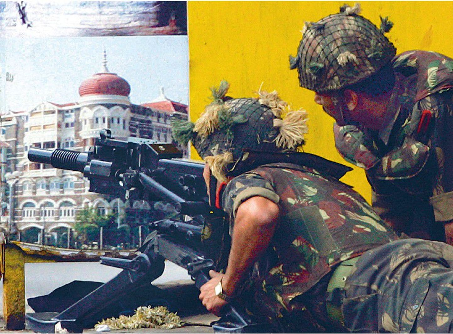 India sõdurid sihivad nurga tagant Taj Mahali luksushotelli granaadiheitjaga. Seinal on hotelli kujutav plakat.