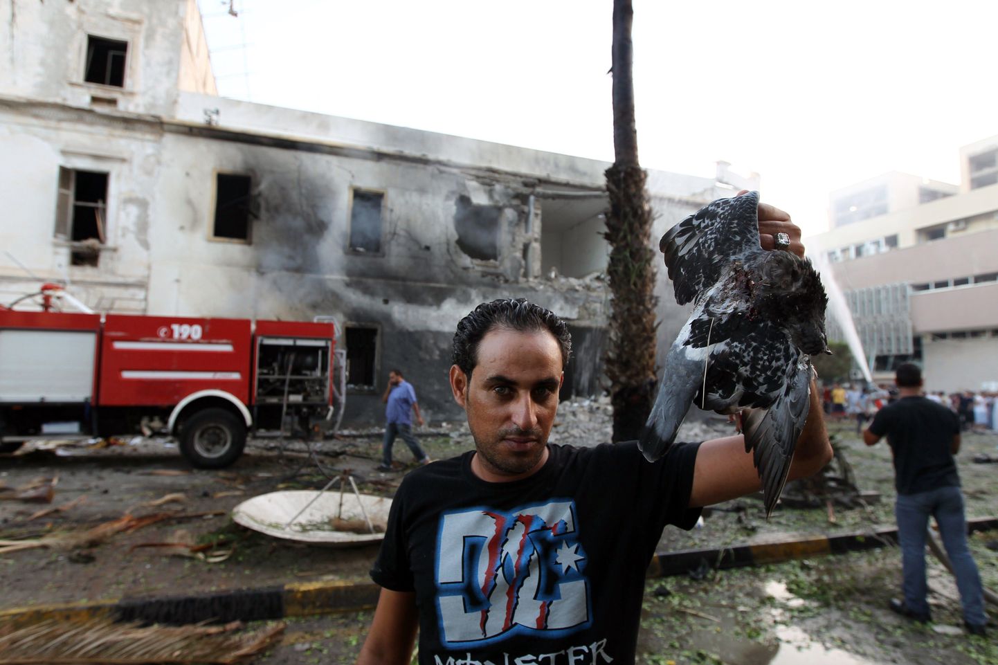 Liibüa mees Benghazis plahvatuses hukka saanud linnuga, taustal suitsev välisministeeriumihoone.