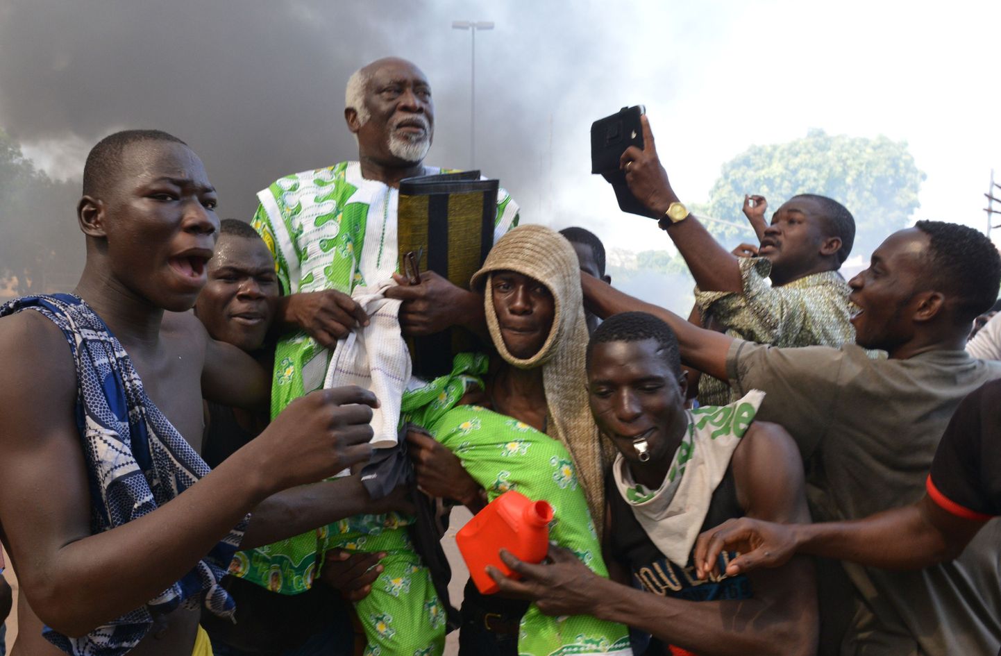 Opositsiooni toetajad kannavad endid esindavat parlamendisaadikut läbi Burkina Faso parlamendihoone põlengust tõusva suitsu.
