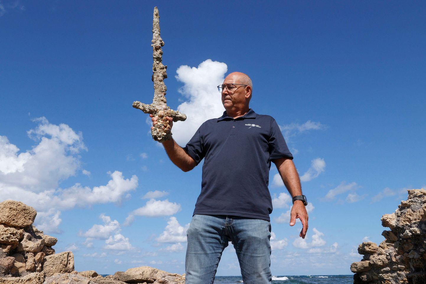 Izraēlas Senlietu pārvaldes Jūras arheoloģijas nodaļas direktors Kobi Šarvits tur atrasto zobenu