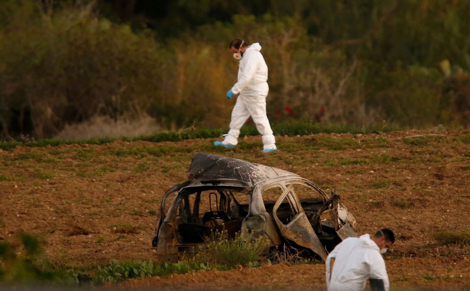 FILE PHOTO: Forensic experts walk in a field after a powerful bomb blew up a car (Foreground) and killed investigative journalist Daphne Caruana Galizia in Bidnija, Malta, October 16, 2017.   To match Special Report MALTA-DAPHNE/CHINA. REUTERS/Darrin Zammit Lupi/File Photo