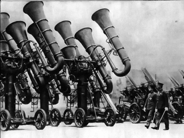 Jaapani keiser Hirohito kontrollib 1936. aastal sõjaväe neljarattalistele kärudele paigaldatudhelipüüdureid. Püüdurid koosnevad kahest ruuporipaarist, üks paar on horisontaalteljel jateine vertikaalteljel. Igast paarist väljuvad kummivoolikud kinnituvad tehniku stetoskoobitüüpikõrvaklappide külge. Stereofoonilist kuulmist kasutades ja pöörates ruuporite telge seni, kunilennuki müra kõlab kõrvaklappides „keskel“, saabki määrata lennuki suunda ja kõrgust.