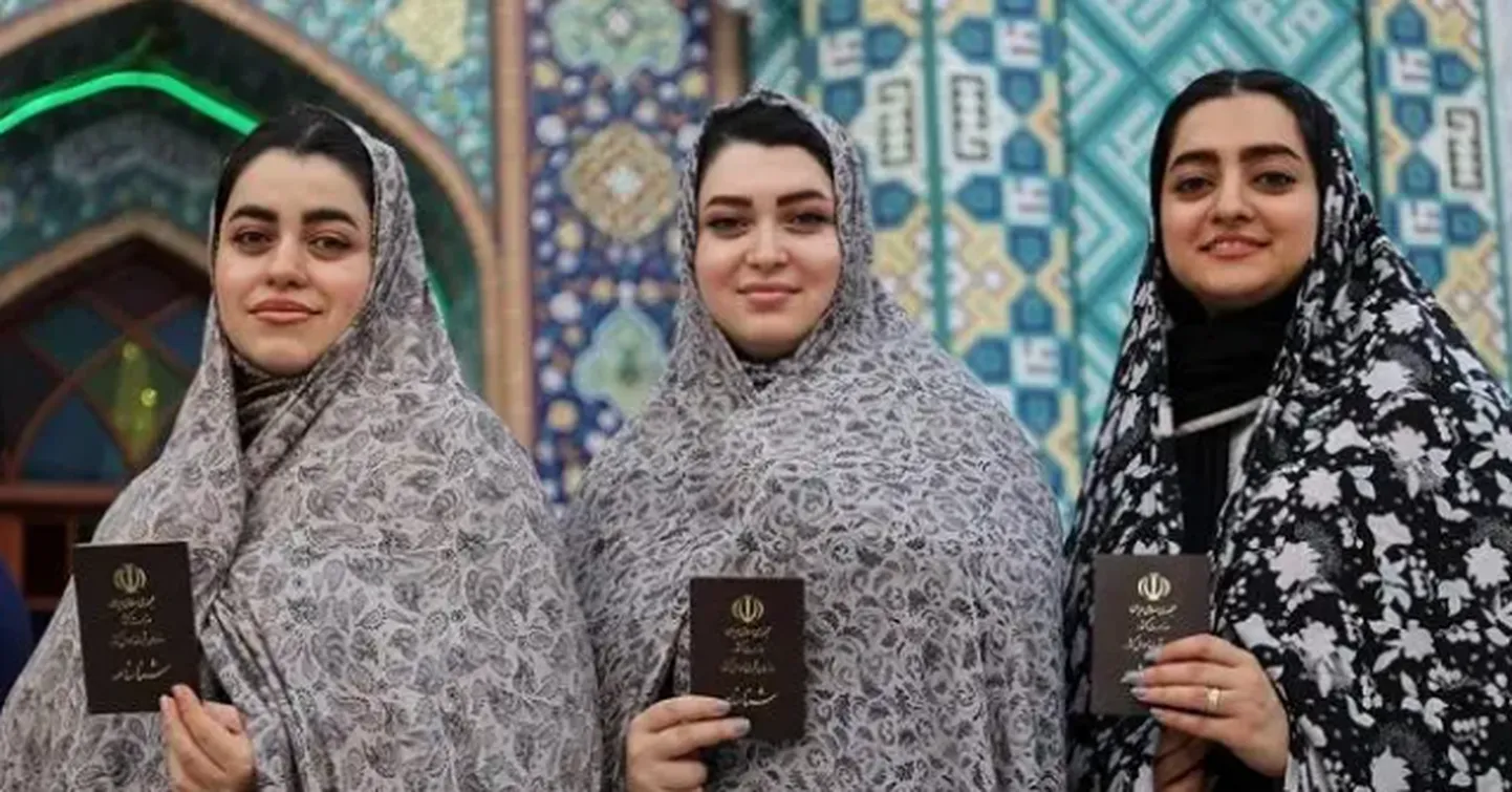 Иранки с документами позируют для фото после голосования в Тегеране в пятницу