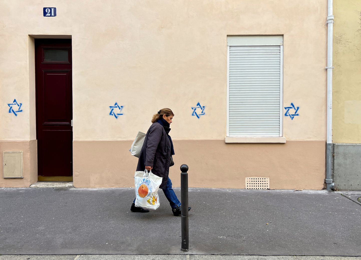 Женщина проходит мимо дома с нарисованными на стене звездами Давида в Париже.