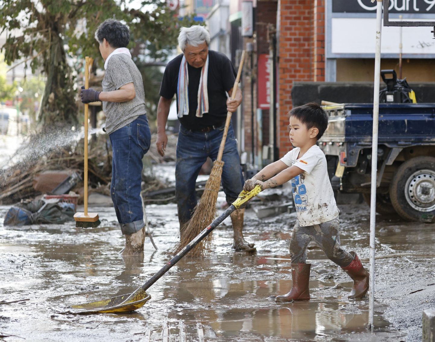 Väike poiss üleujutatud Kumamoto preferaktuuris, aitamas oma vanavanematel maja esist puhastada.