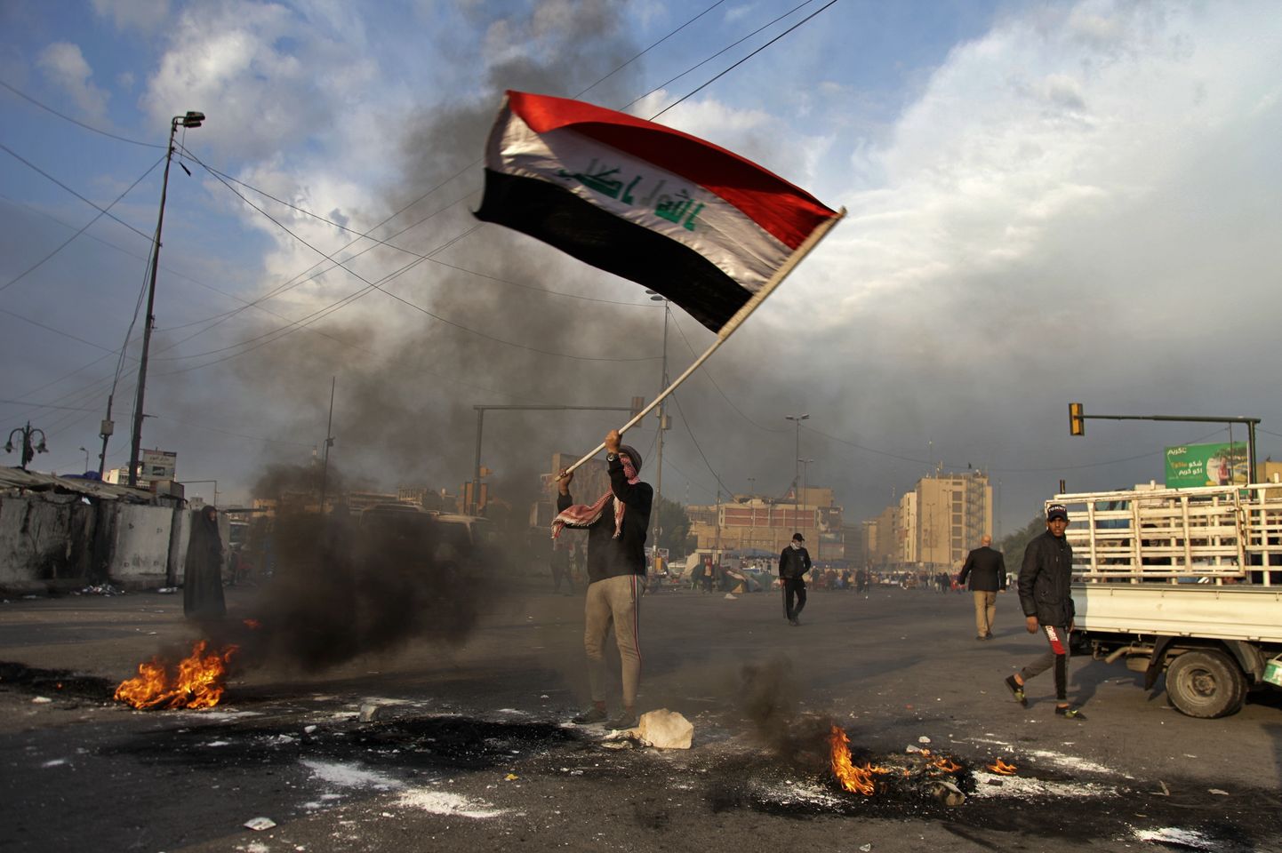 A protester waves the national flag while demonstrators set fire to close streets near Tahrir Square during a demonstration against the Iranian missile strike in Baghdad, Iraq, Wednesday, Jan. 8, 2020.