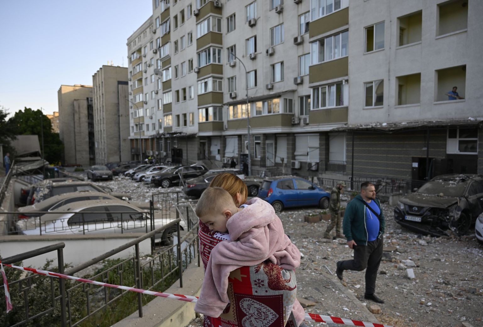 30 мая 2023 года, Киев. Женщина несет своего ребенка возле многоэтажного жилого дома, поврежденного осколками от сбитого беспилотника-камикадзе российской армии.