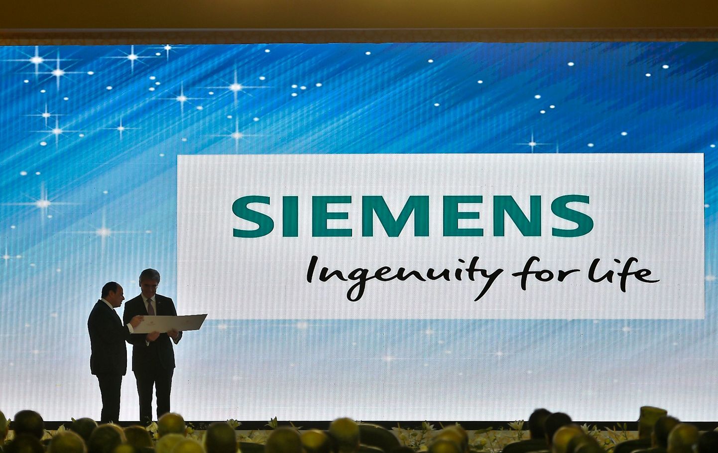 Egyptian President Abdel Fattah al-Sisi (L) and Joe Kaeser (R) the CEO of German engineering giant Siemens look at a document during the inauguration of three large power plants as well as other projects in the energy sector, on the outskirts of the capital Cairo on July 24, 2018. 
The Egyptian President inaugurated energy projects across the country as Egypt gains an electricity production surplus, after years of power cuts that peaked in 2014. The stations, built by Siemens company, include "the largest air-cooled station in the world" in the new capital, said Electricity Minister Mohammed Shaker. / AFP PHOTO / KHALED DESOUKI