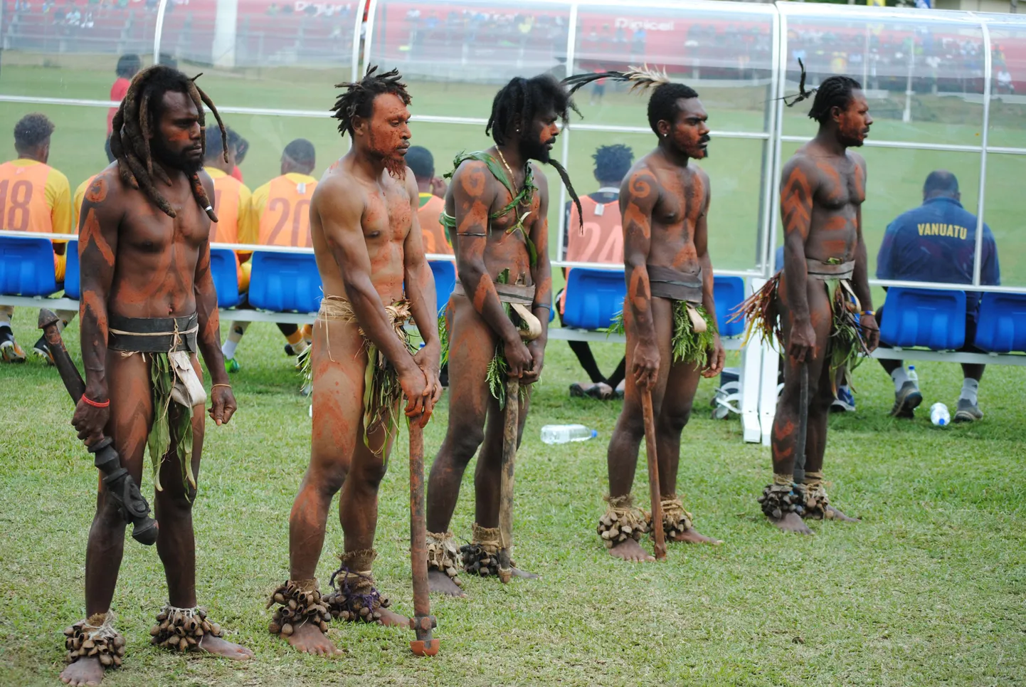 Vanuatu – Eesti A-maavõistlus jalgpallis. Vanuatu koondise vahetuspingi taga seisavad auvalves rahvariietes kohalikud.