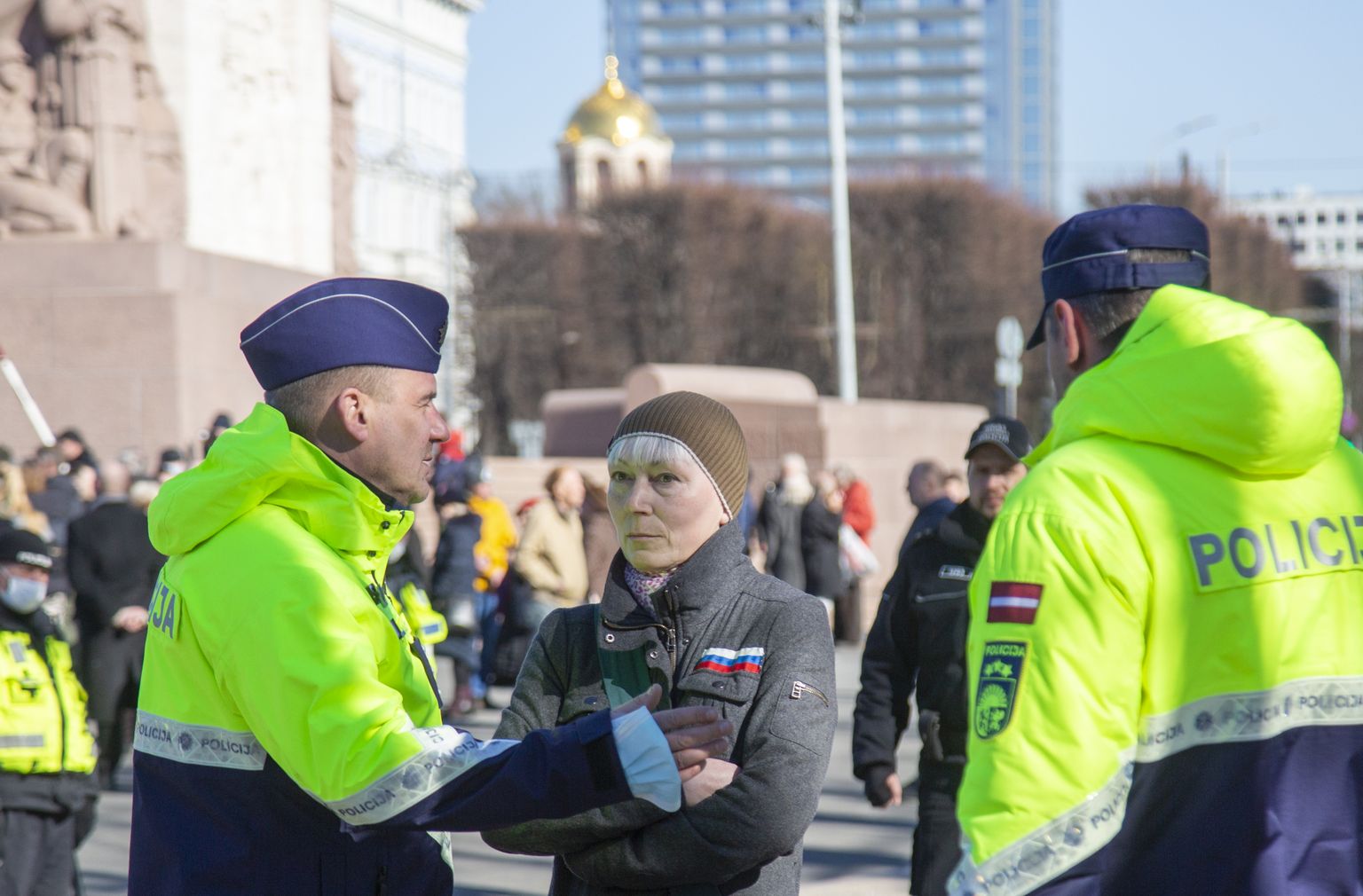 Valsts policijas darbinieki leģionāru gājiena laikā pie Brīvības pieminekļa aiztur sievieti, kuras apģērbu rotā pie krūtīm piešūts Krievijas karodziņš un kura pēdējās dienās kļuvusi populāra sociālajos tīklos, jo apmeklēja veikalu, nesot iepirkumu somu ar Krievijas armijas karā pret Ukrainu izmantoto simbolu "Z".