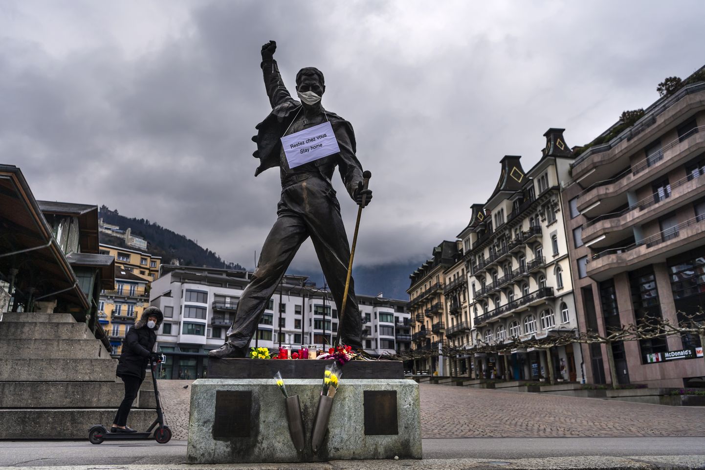 Freddy Mercury kujul Šveitsis Montreux's on näomask ja kaelas silt "jääge koju".