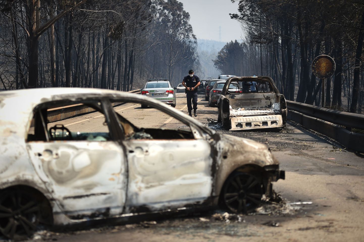TOPSHOT - A policeman walks on a road past burnt cars after a wildfire in Figueiro dos Vinhos  on June 18, 2017.
A wildfire in central Portugal killed at least 57 people and injured 59 others, most of them burning to death in their cars, the government said on June 18, 2017. Several hundred firefighters and 160 vehicles were dispatched late on June 17 to tackle the blaze, which broke out in the afternoon in the municipality of Pedrogao Grande before spreading fast across several fronts.    / AFP PHOTO / PATRICIA DE MELO MOREIRA