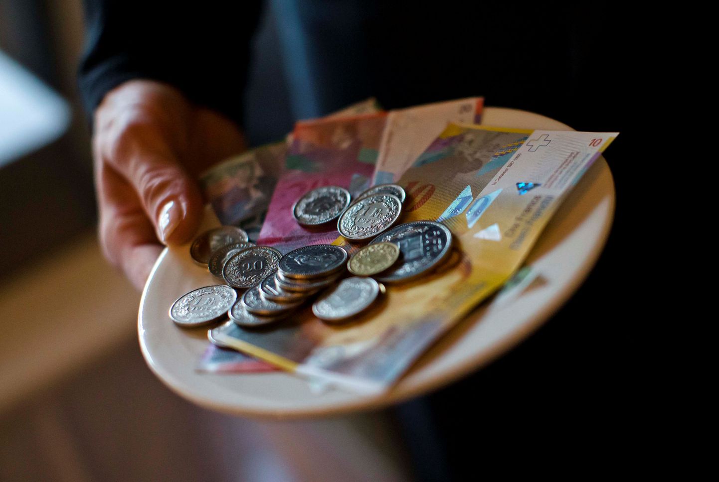 A waitress presents a plate with various Swiss Franc coins and notes in this picture illustration in a restaurant in Zurich, Switzerland, May 21, 2013.   REUTERS/Michael Buholzer/Illustration/File Photo