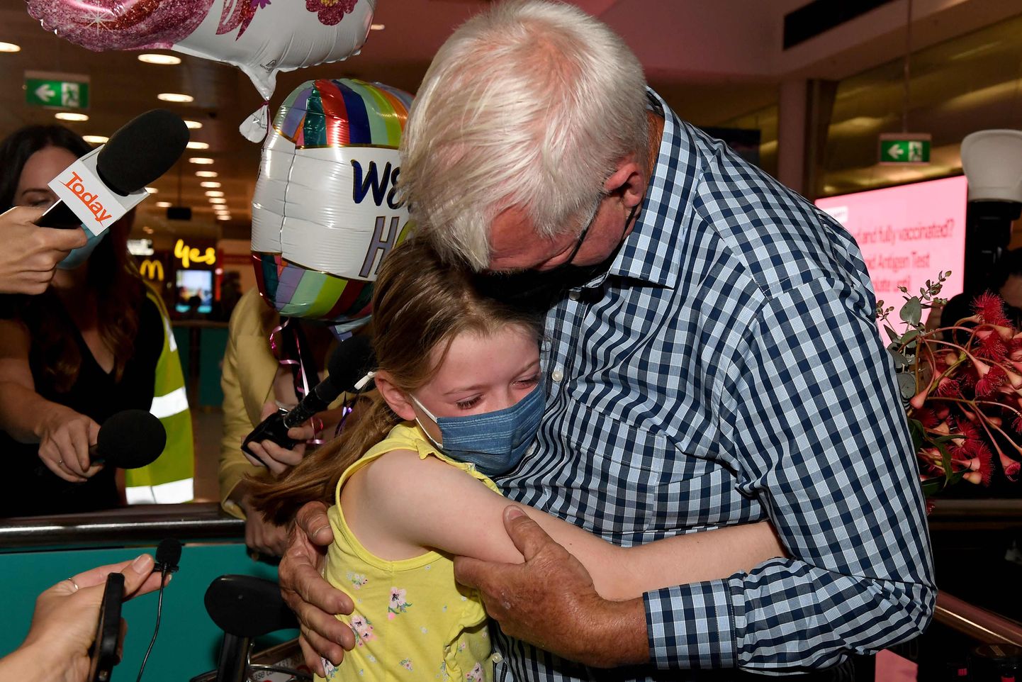 Mees kallistamas Austraalia Sydney lennujaamas 21. veebruaril 2022 oma lapselast. Pildil on näha ka ajakirjanikke, kes tahavad neid intervjueerida