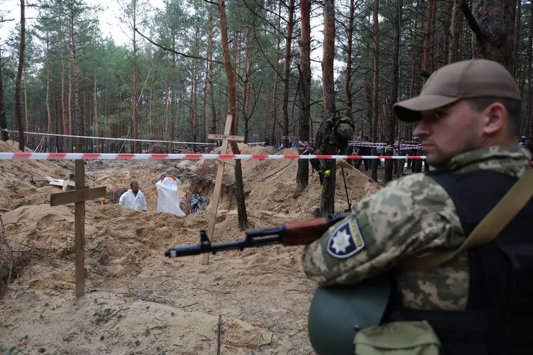 Украинский полицейский охраняет братскую могилу в Изюме.