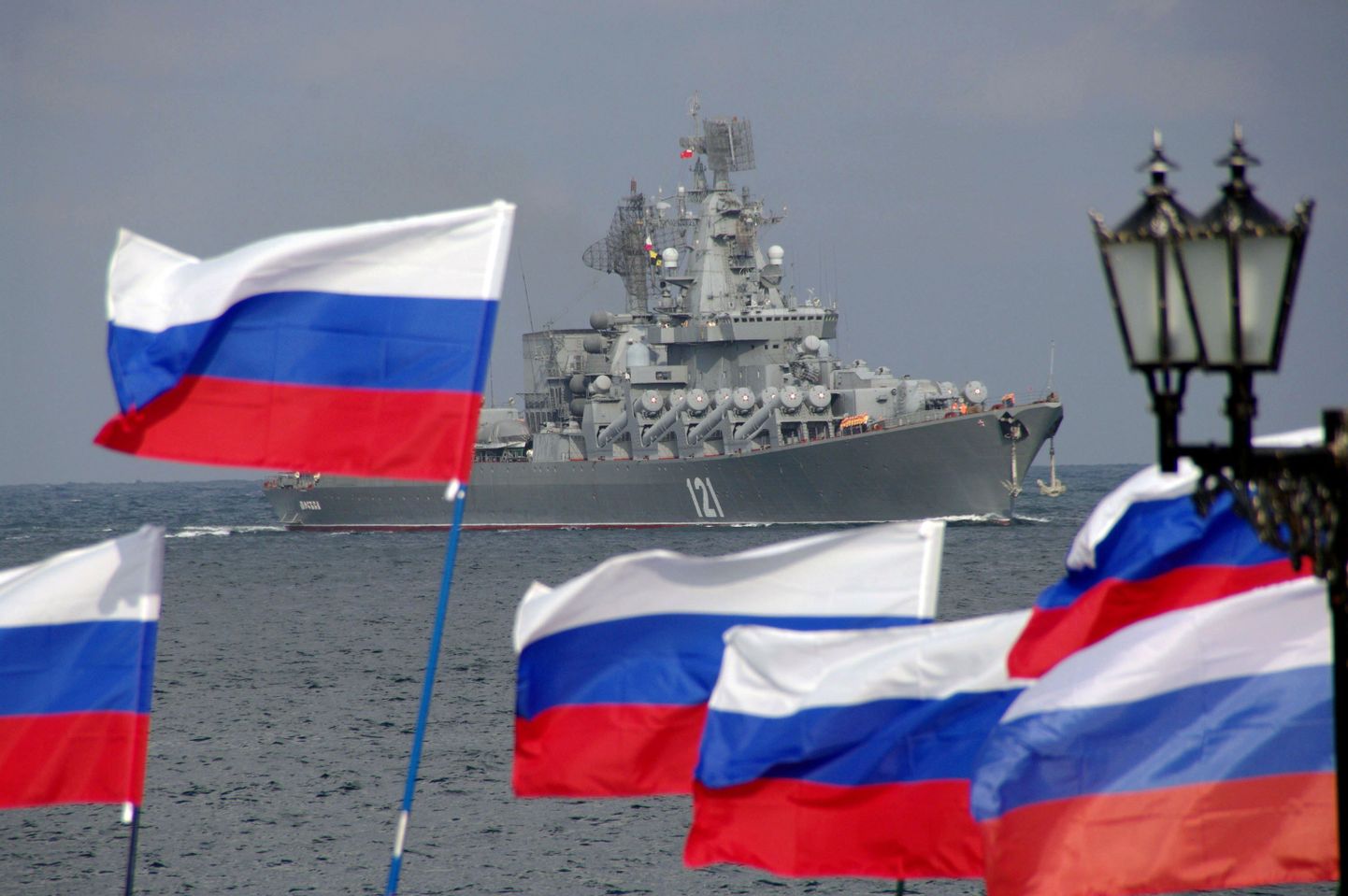 Ракетный крейсер на фоне российских флагов.