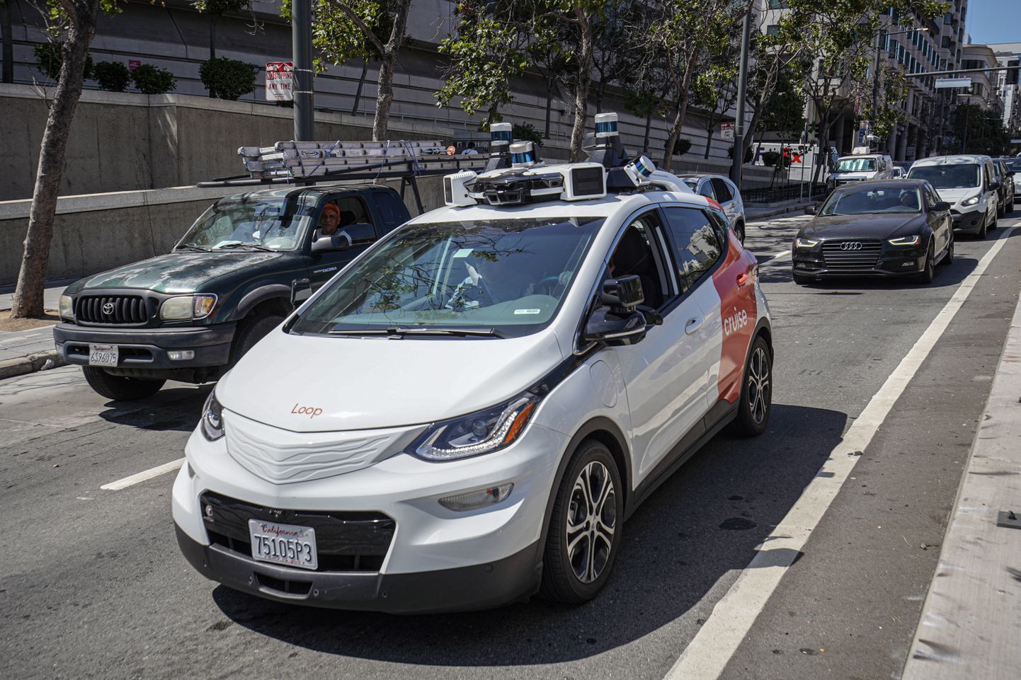 Isesõitev takso vuramas San Francisco tänaval 2023. aasta augustis. Robottakso teenust pakuvad linnas kaks ettevõtet Waymo ja Cruise, kes on ajanud oma töökohtade pärast muretsevad taksojuhid taustal mässama.