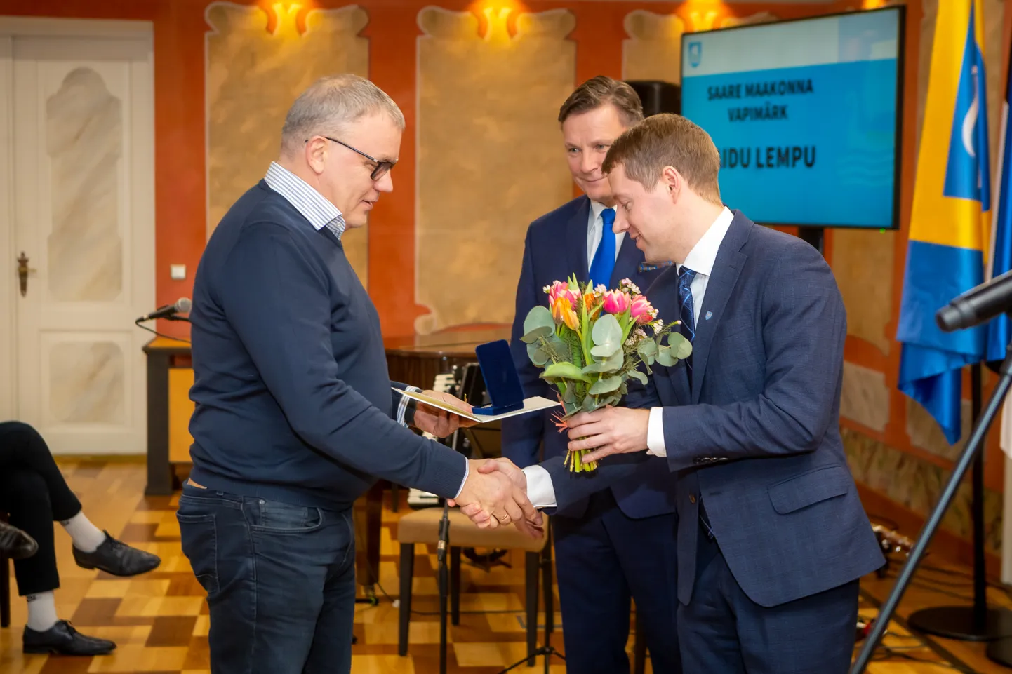 Maidu Lempul surub kätt ja ulatab lilled vallavanem Mikk Tuisk. Assisteerib volikogu esimees Jaanus Tamkivi.