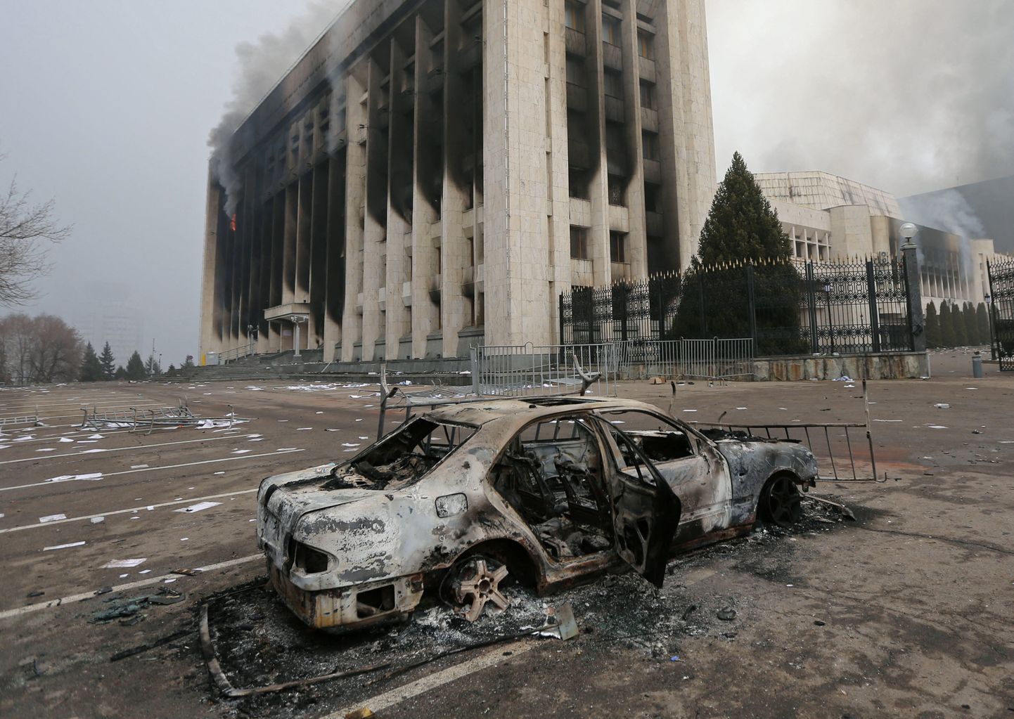 Süüdatud auto, taamal Almatõ linnapea hoone, mis pandi hiljutiste meeleavalduste käigus põlema.