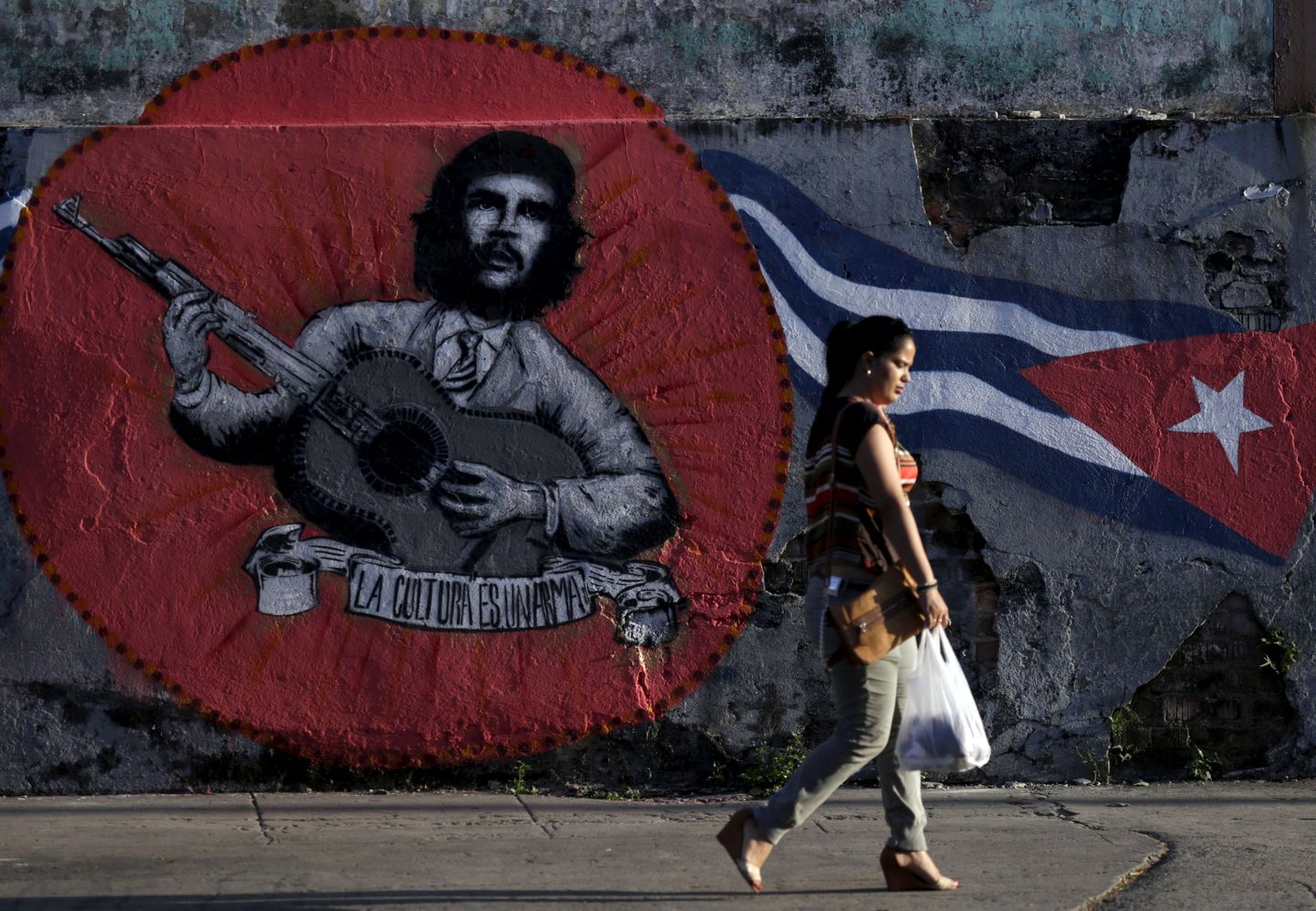 Naine kõndimas mööda seinale kantud grafitist, millel on kujutatud Ernesto «Che» Guevara ja Kuuba lipp