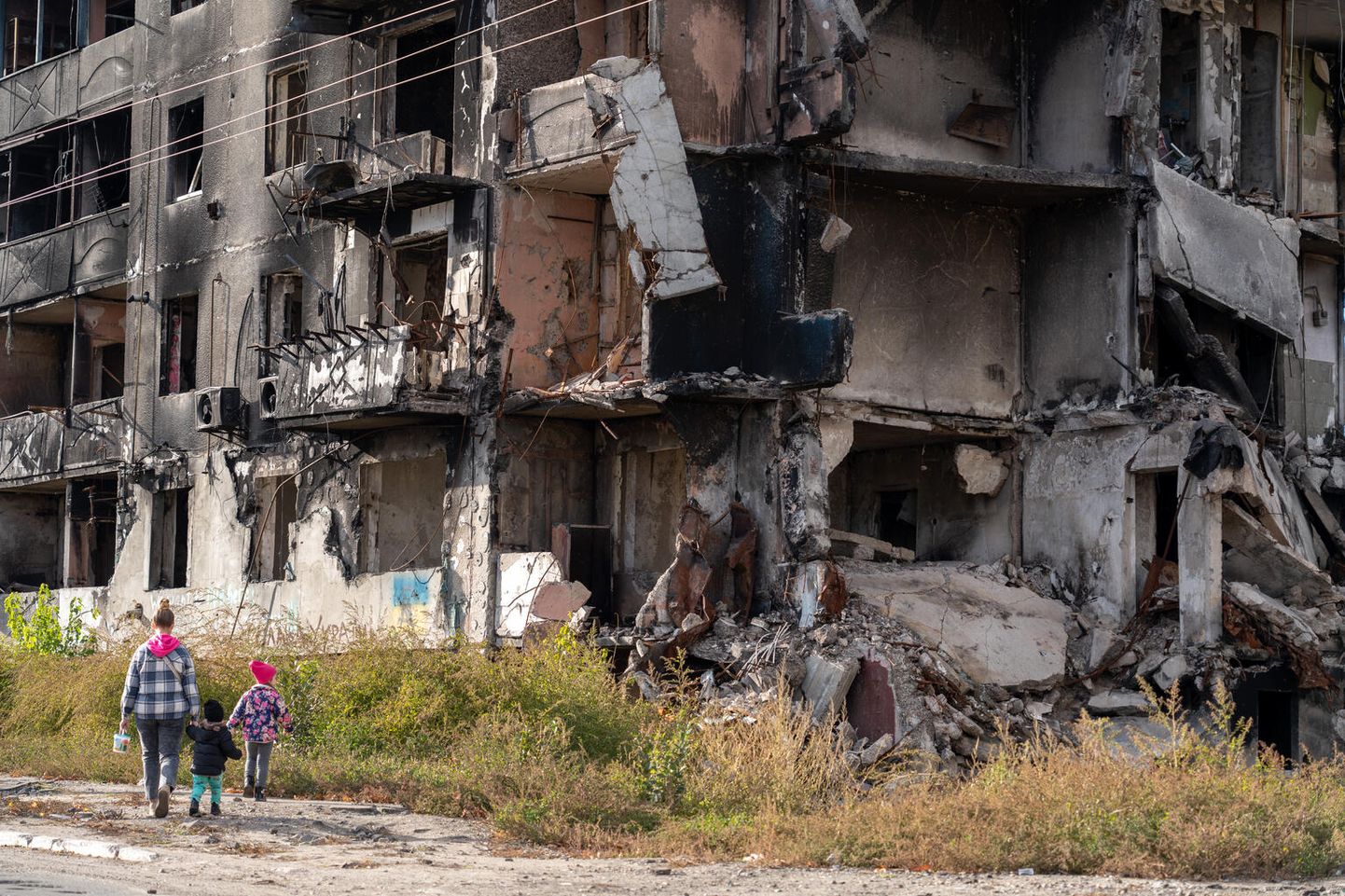Мать с детьми идет мимо разрушенного в результате ракетных обстрелов России дома на Бородянке, Украина, октябрь 2022 года.