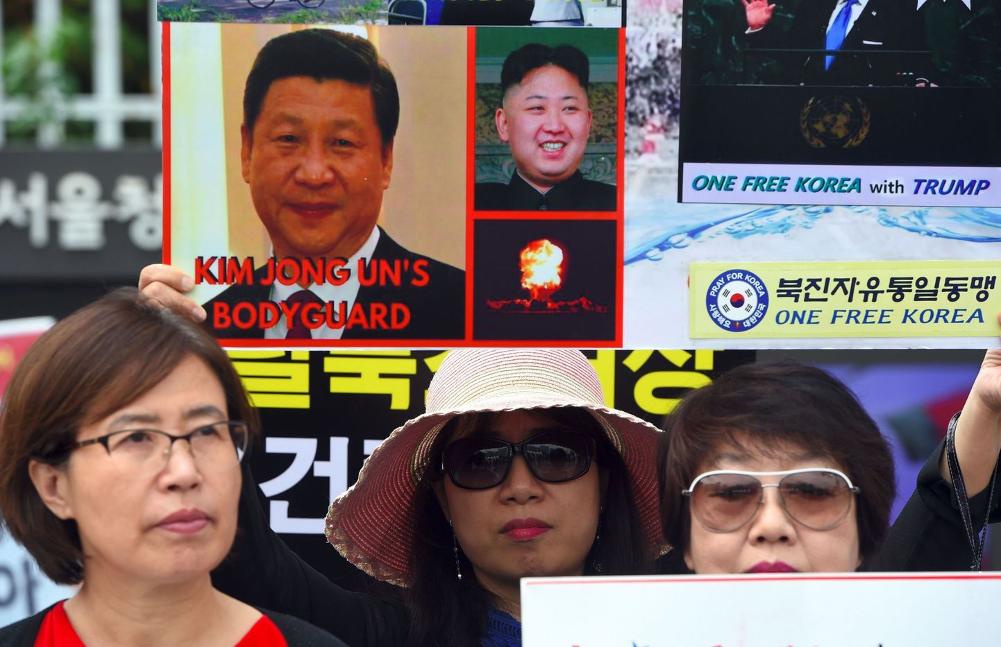 Põhja-Koreast põgenenud inimesed hoidmas plakatit, mis süüdistab Xi Jinpingi Kim Jong-uni ihukaitsja olemises.
