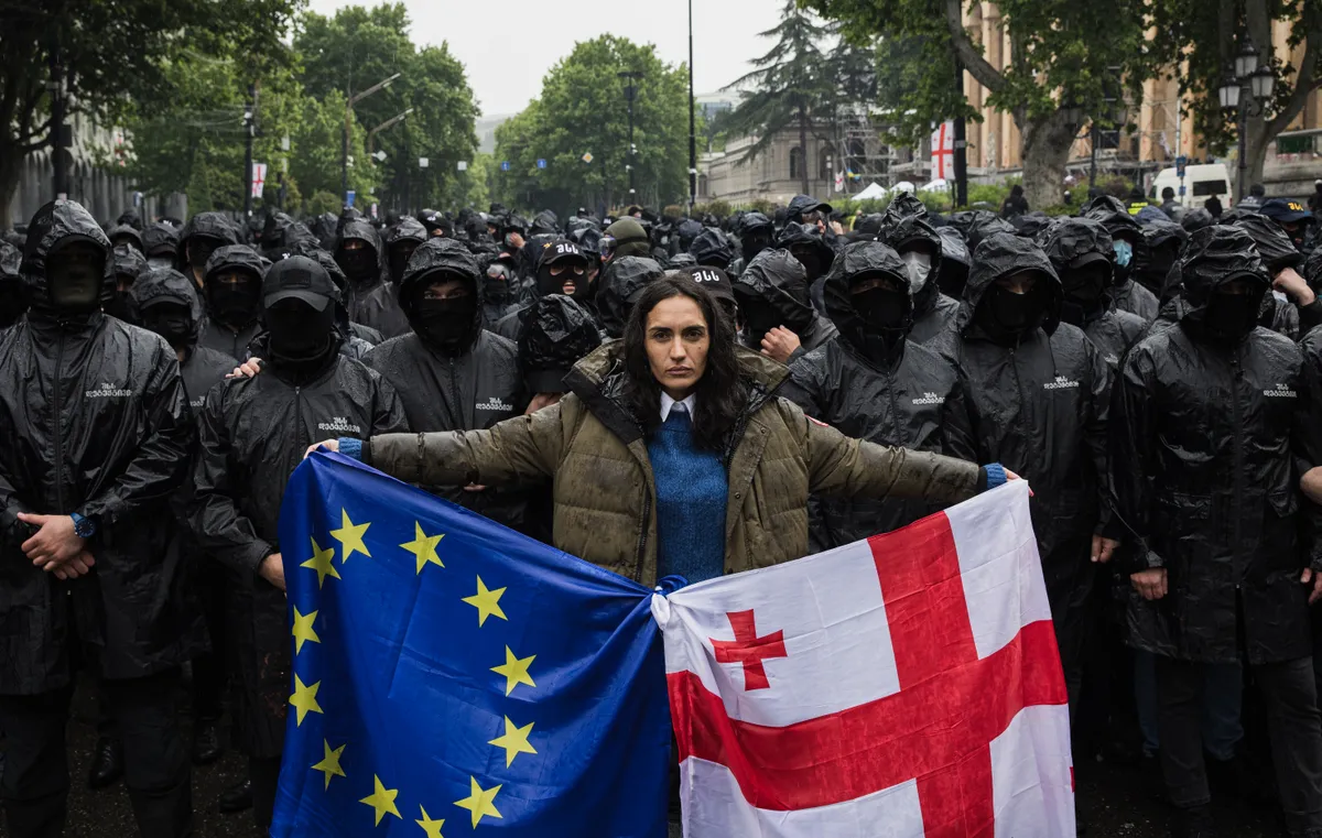 A Georgian woman stands in the heart of Tbilisi, confronting hundreds of police officers, with the European Union and Georgian flags intertwined in her hands. The people aspire to align with Europe, while the nation’s oligarchic leaders gravitate towards Russia.