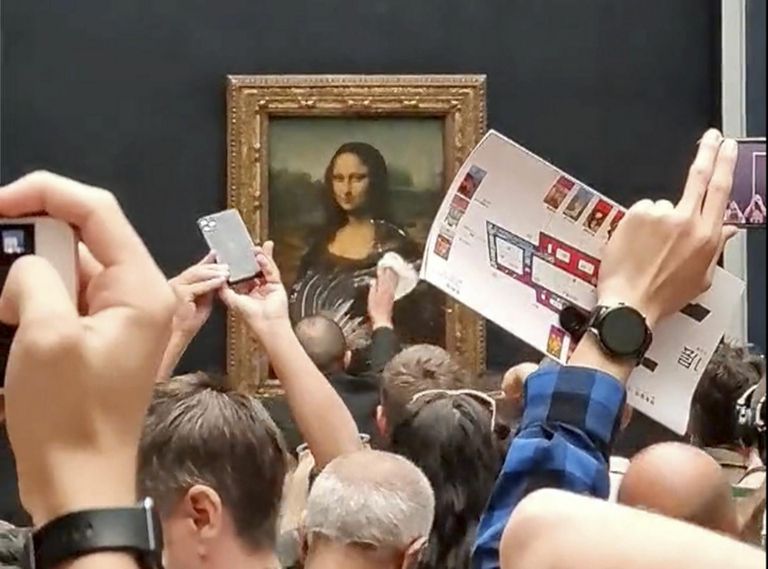 End vanaks ratastoolis naiseks maskeerinud aktivist määris maikuus «Mona Lisa» kokku koogiga. Pildil püüab muuseumitöötaja seda puhastada, samal ajal kui turistid pilte teevad. 