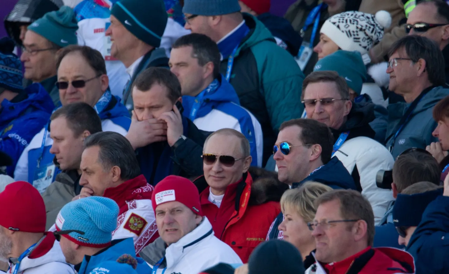Президент ЭОК Нейнар Сели (в левом верхнем углу, в солнцезащитных очках) наблюдает с трибуны за воскресной мужской лыжной эстафетой рядом с Владимиром Путиным и премьером Дмитрием Медведевым (в центре).