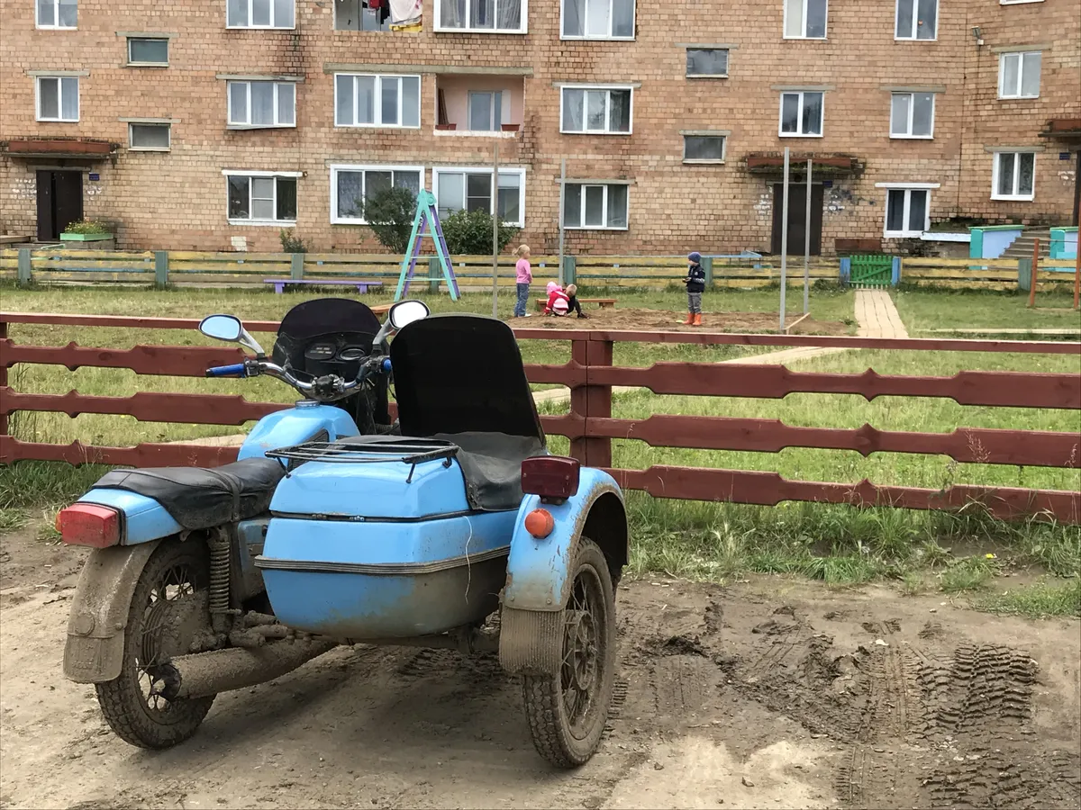 Kohalikel teedel on korviga tsikkel IŽ-Jupiter kõva tegija. Antud eksemplar on pargitud 8000 elanikuga Tajožnõi asula keskuses asuva viiekorruselise kortermaja ette. Püüdmist ei saa kohalikele ette heita, mida tõestab ka antud oludes mõnus mänguväljak, mille peamine pluss on suurus ja täielik murukate. Maja enamus aknaid on uued ja plastikust. Hoovis kohtasin tunkedes Aasia-päritolu mehi, kes küsimusele, kust nad on ja mis tööd teevad siin kauges Siberi asulas, kiiresti lahkusid ja maja ühte trepikotta sisenesid. Lahke kohalik pensionärist mammi seletas, et tegemist on töölistega Põhja-Koreast, kes pidid kusagil ehitusel töötama ning võõrastega polevat neil lubatud rääkida.