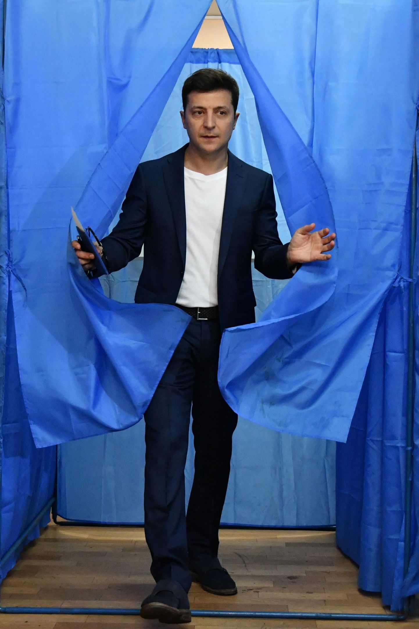 Volodõmõr Zelenskõi astumas välja Kiievi valimisjaoskonnas hääletuskabiini lipusiniste kardinate vahelt.
