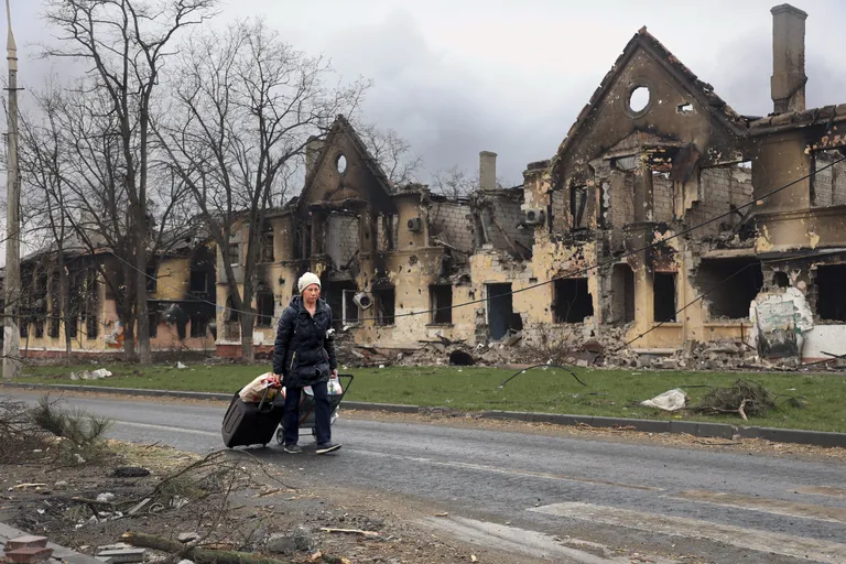 Sõjas purustatud maja ja põgenev naine Mariupolis.