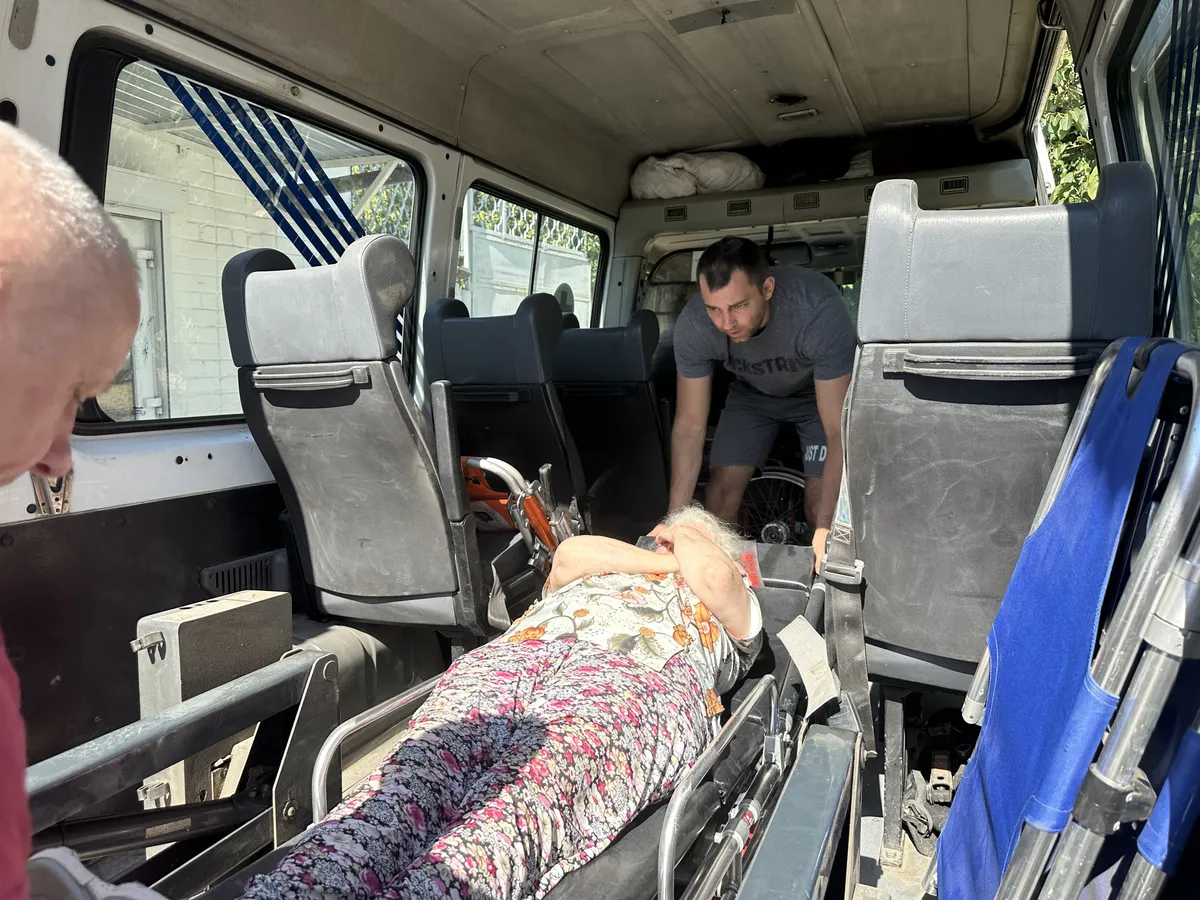 A Kherson volunteer evacuation team unloads another survivor from their minibus, which has narrowly escaped drone attacks multiple times. The latest evacuee is 83-year-old Ludmilla. The stretcher is held by Konstantyn, the main hero of our story.