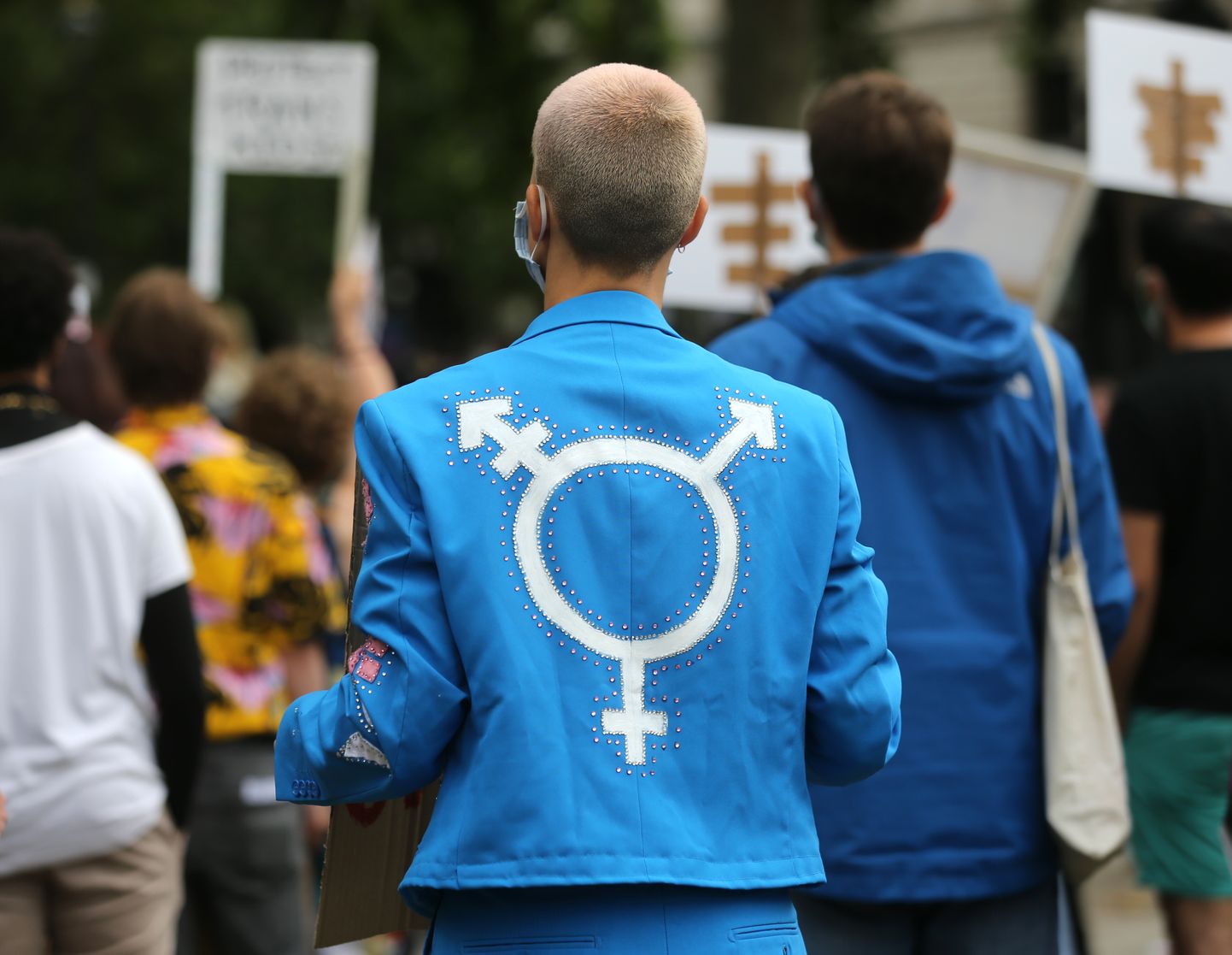Демонстрант в ярко-синей куртке с изображением гендерно-нейтрального символа. Иллюстративное фото.