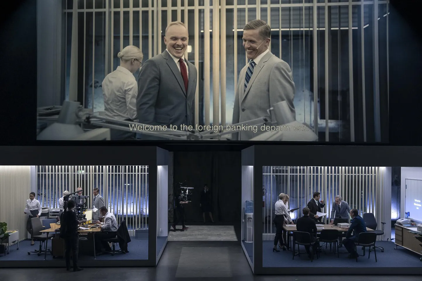 Tegevus pangakontoris on kaamerate vahendusel kuvatud suurele ekraanile, kus on näha vestlemas Oliveri (Karmo Nigula, vasakul) ja Arturit (Tõnis Niinemets).