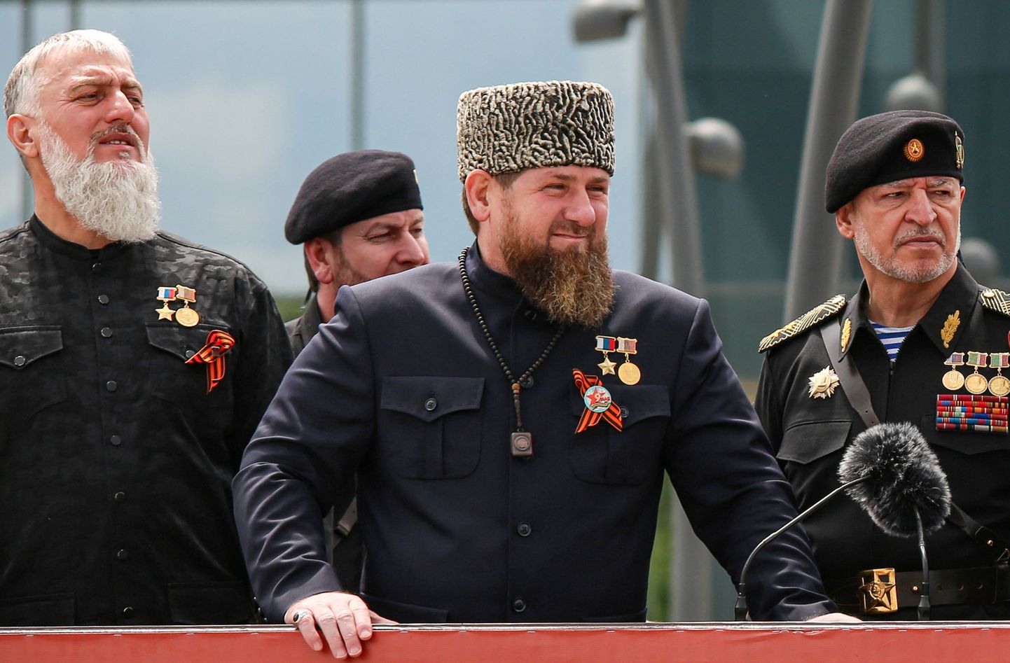 Адам Делимханов (слева) стоит на трибуне с главой Чечени Рамзаном Кадыровым и другими представителями силовых структур региона, Грозный, 9 мая 2022 года.