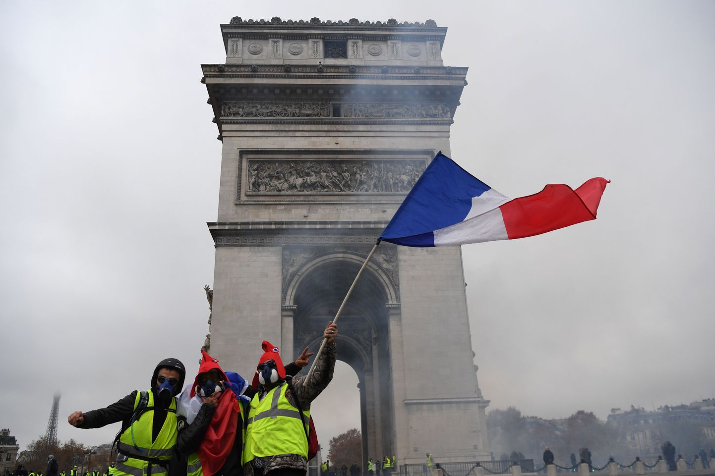 Demonstrators pose with a French flag with the Arc de Triomphe in background during a protest of Yellow Vests (Gilets jaunes) against rising oil prices and living costs on the Champs Elysees in Paris, on December 1, 2018. - Thousands of anti-government protesters are expected today on the Champs-Elysees in Paris, a week after a violent demonstration on the famed avenue was marked by burning barricades and rampant vandalism that President Emmanuel Macron compared to "war scenes". (Photo by Alain JOCARD / AFP)