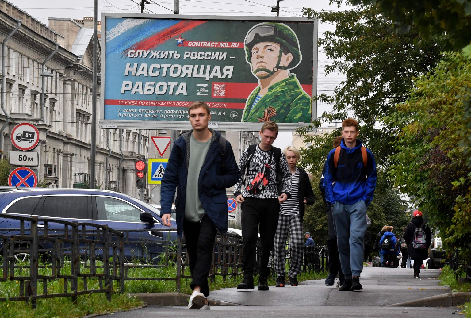 Молодые люди проходят перед рекламным щитом с изображением военнослужащего и лозунгом «Служить России — это настоящая работа» в Санкт-Петербурге, 29 сентября 2022 года.