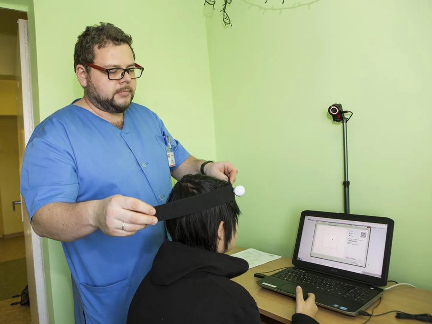 Tegevusjuhendaja Andres Linnupuu näitab, kuidas patsiendile andur pea külge kinnitatakse. Tegelikult teeb seda uuringut õde.