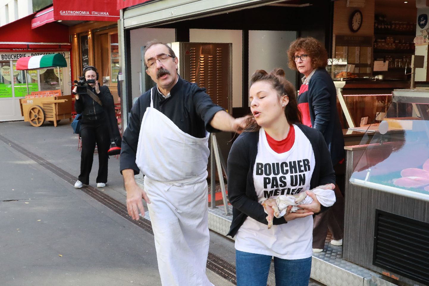 Французский мясник пытается прогнать от дверей магазина веганского активиста с маленьким мертвым поросенком в руках.