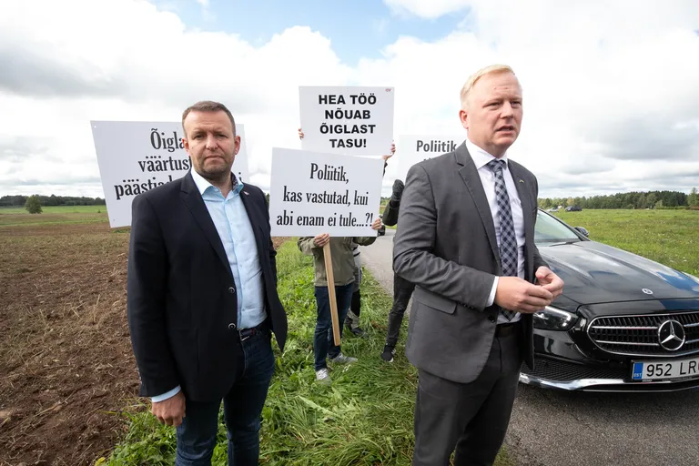 Глава МВД Ляэнеметс и министр финансов Вырклаэв не улыбаются журналистам на фоне протестующих жителей Эстонии, Вихула, 2020 год.