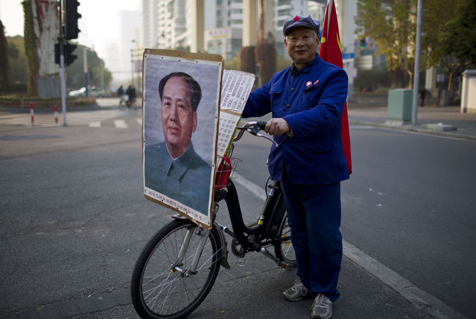 Punaarmee mütsiga endine laevatehase töötaja poseerimas Mao Zedongi plakatiga rattaga.