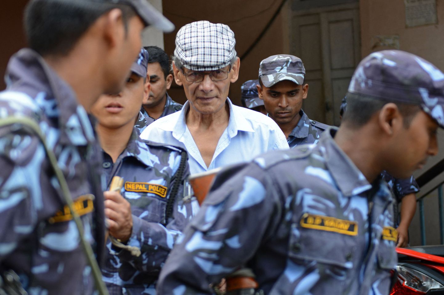 Sel 2014. aasta 12. juunil Bhaktapuris tehtud fotol toimetab Nepali politsei Prantsuse sarimõrvari Charles Sobhraji ringkonnakohtusse istungile, kus arutati Kanada seljakotireisija Laurent Ormond Carriere'i mõrva.