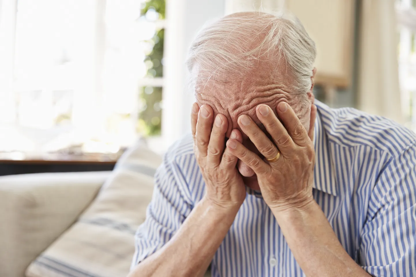 Senior Man Sitting On Sofa At Home Suffering From Depression