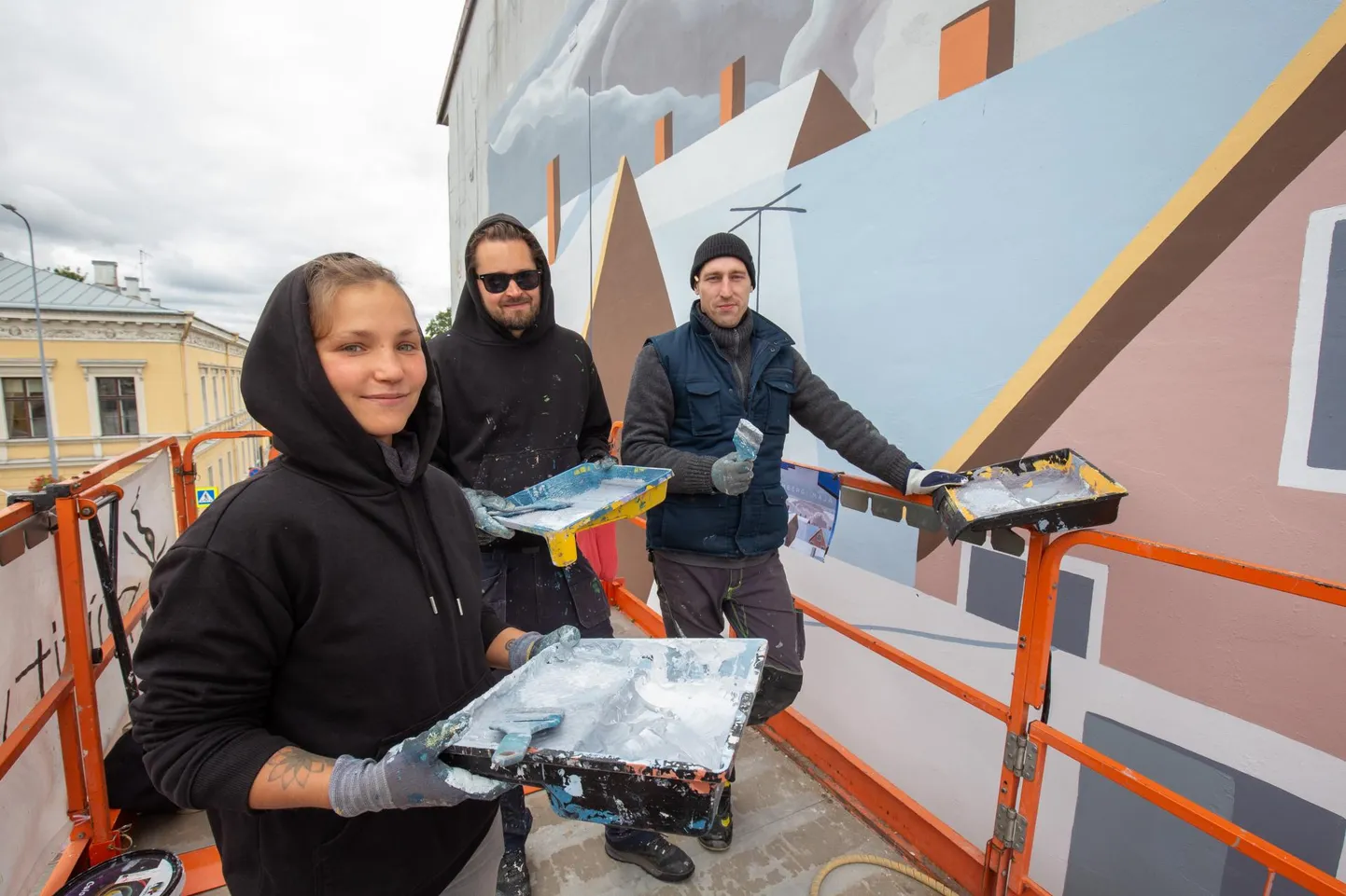 Kunstnikud Regina-Mareta Soonsein, Edgar Tedresaar ja Alar Tuul maalivad kergelt kõikuval tõstukiplatvormil Tallinna tänava hoone seina.