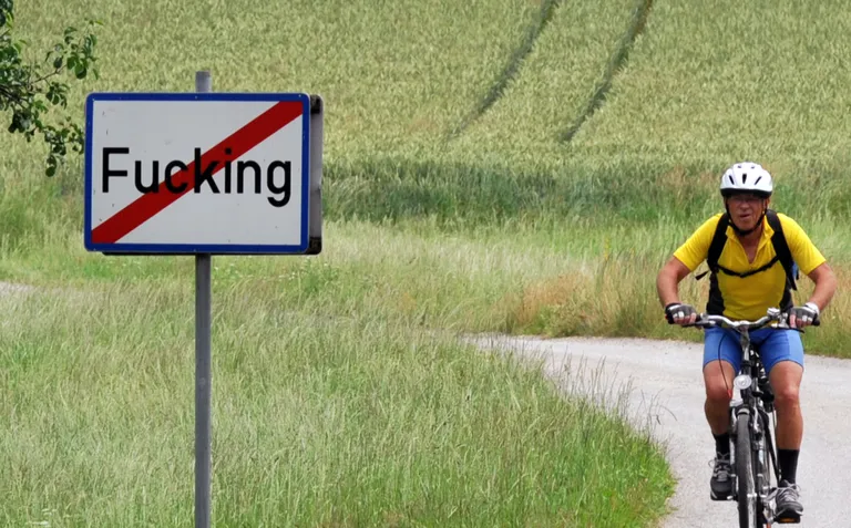 Jalgrattur sõitmas sildi juures, mis näitab, kus lõppeb ja algab Austria küla Fucking