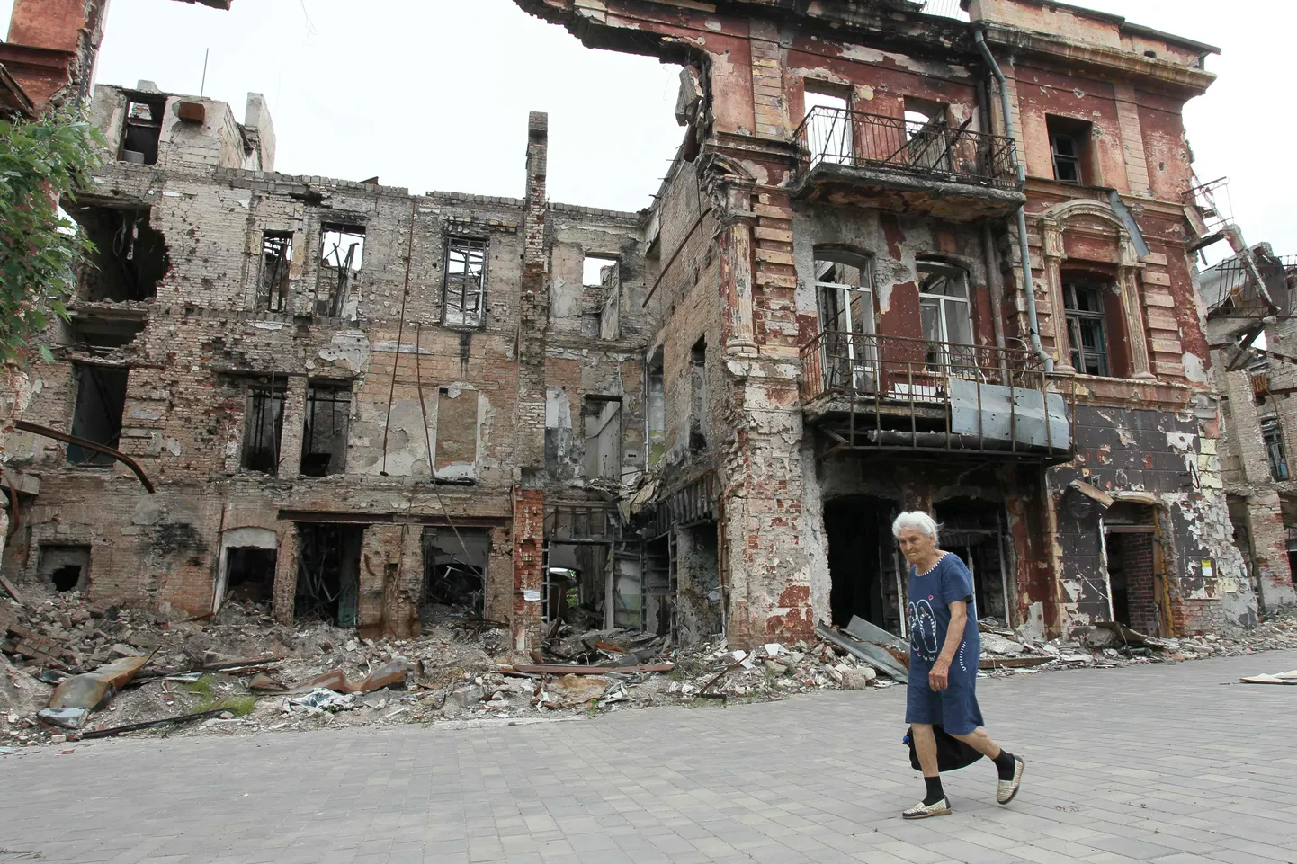 Naine möödub tänavu juunis Mariupolis purustatud majast. Suurem osa kesklinnast on jätkuvalt rusudes.