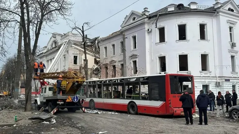 Последствия удара по Сумам. На переднем плане уничтоженный автобус, на заднем - разрушенное здание корпуса университета