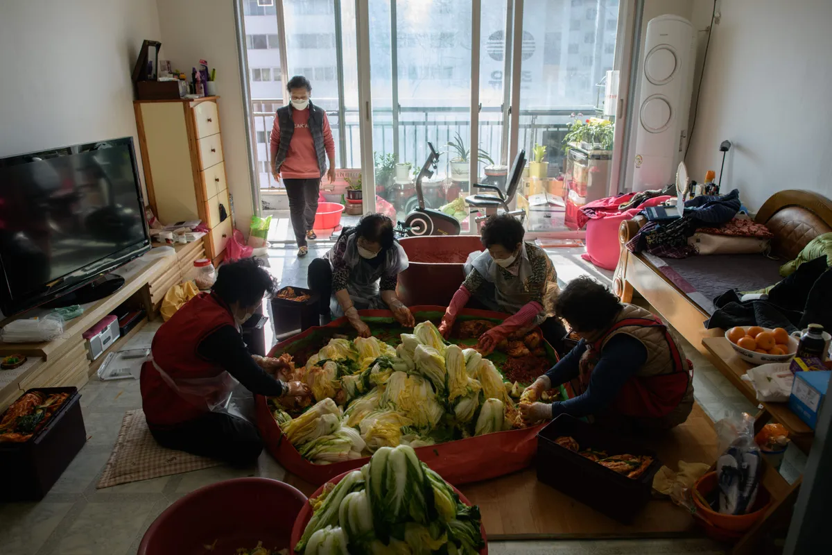 Draugi gatavo kimči. Šo tradicionālo pasākumu dēvē par "kimjang". Kā redzams, tas notiek mājās, viesistabā.
